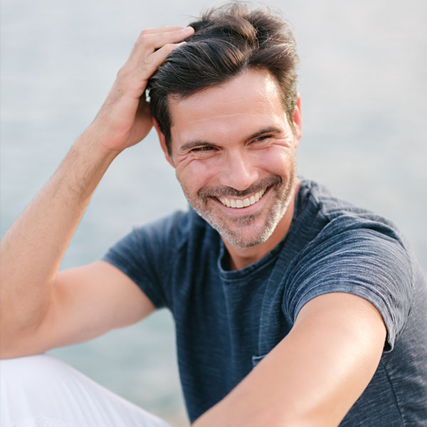 A relaxed man smiling confidently near the water, reflecting the comfort and assurance that come with expert dental care - dentist marion ma